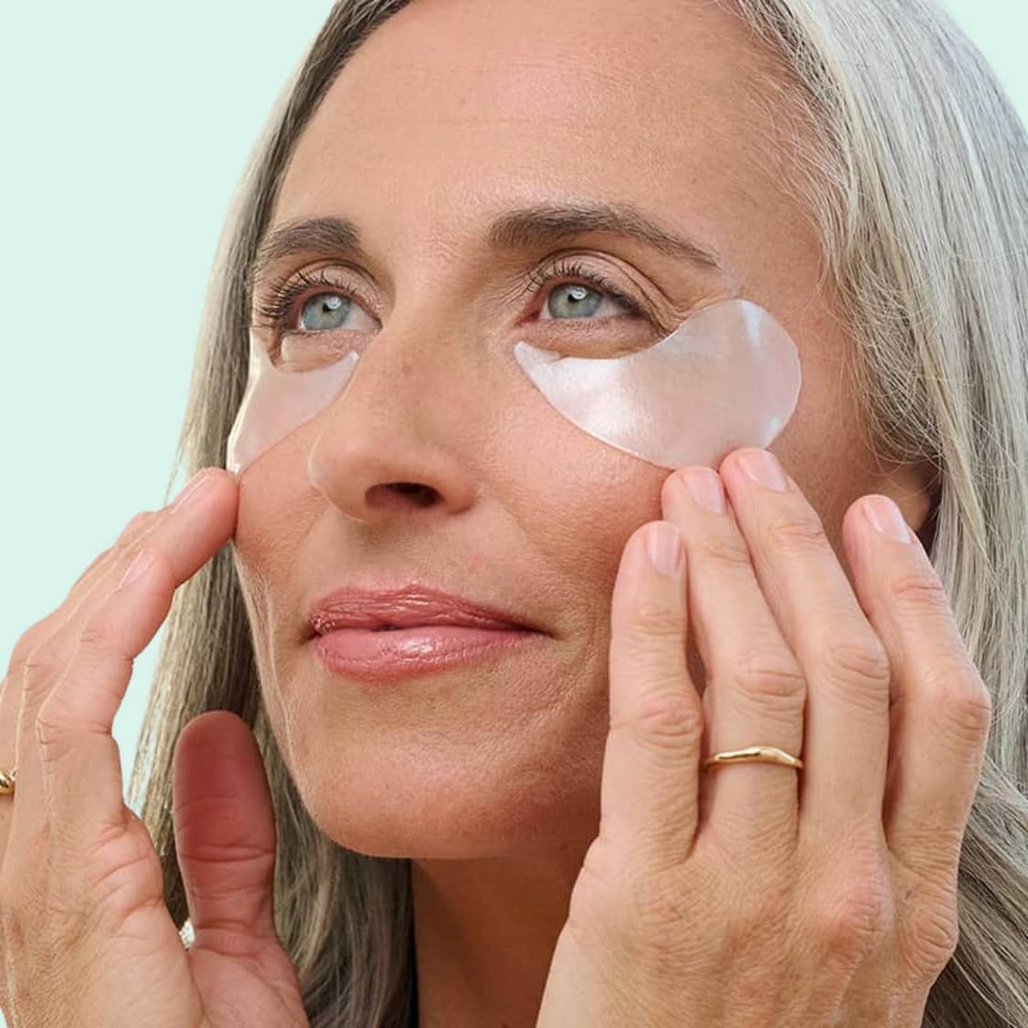 Woman applying top-rated rejuvenating patches under her eyes with a light green background