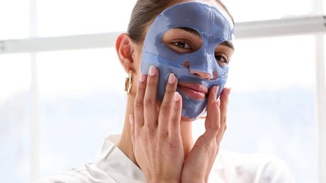 Woman applying blue gel face mask with hands for detoxifying skincare treatment