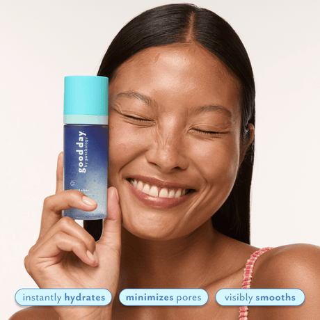 A smiling woman with closed eyes holds a blue and turquoise Good Day skincare bottle next to her face against a light background, with text overlays at the bottom reading 'instantly hydrates', 'minimizes pores', and 'visibly smooths'.