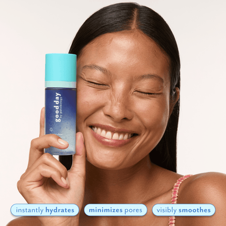 A smiling woman with closed eyes holds a blue and turquoise Good Day skincare bottle next to her face against a light background, with text overlays at the bottom reading 'instantly hydrates', 'minimizes pores', and 'visibly smooths'.