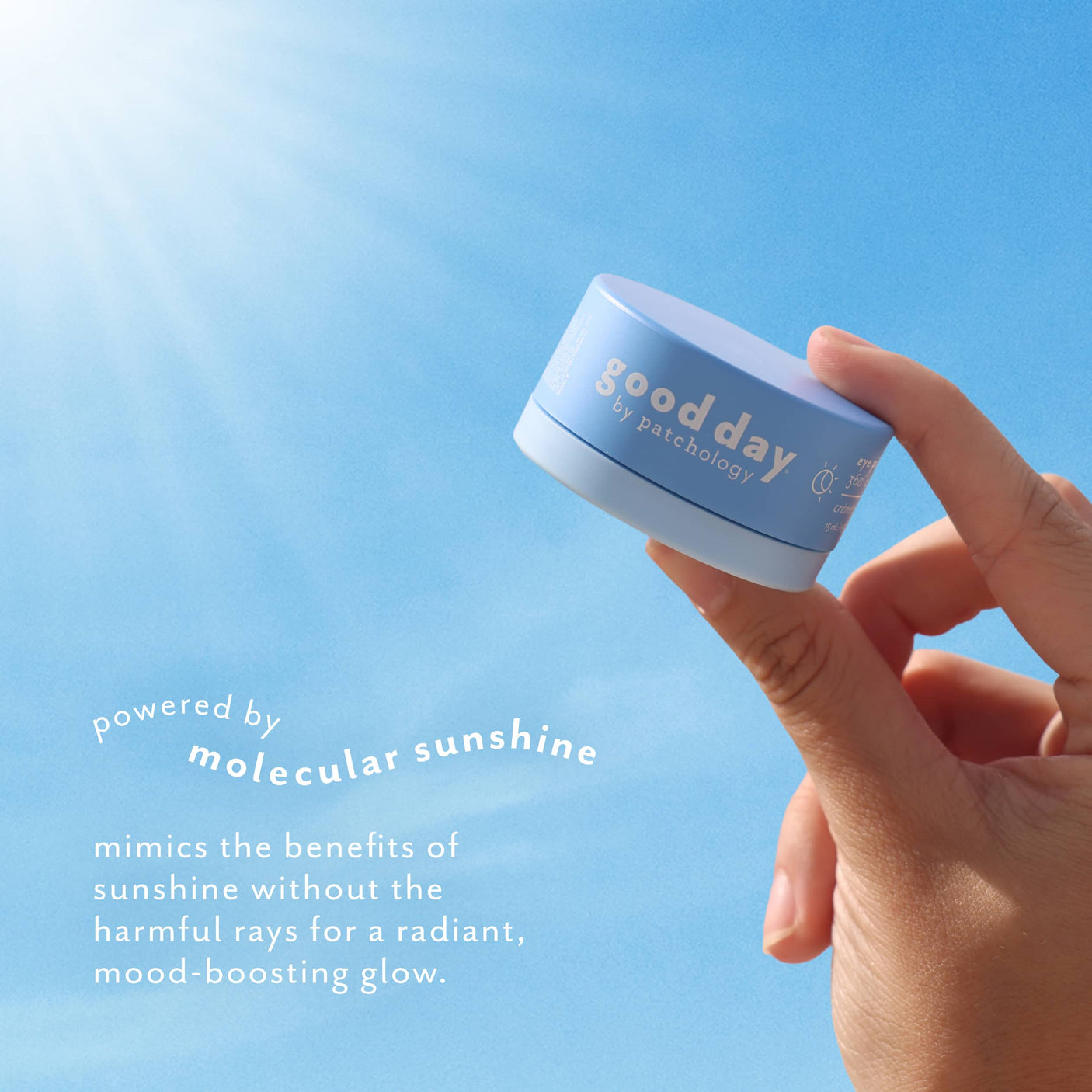 Hand holding Eye Pillow 360° Brightening Eye Cream against a bright blue sky, highlighting molecular sunshine for a radiant, mood-boosting glow.