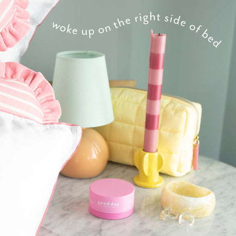 Nine-to-Five Instant Wake-Up Morning Gel-Cream on a bedside table with a lamp, striped candle, yellow bag, and jewelry.