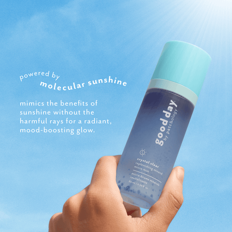 A hand holds a bottle of Good Day 'Crystal Clear' hydrating mist against a bright blue sky background with text overlays describing its molecular sunshine technology.