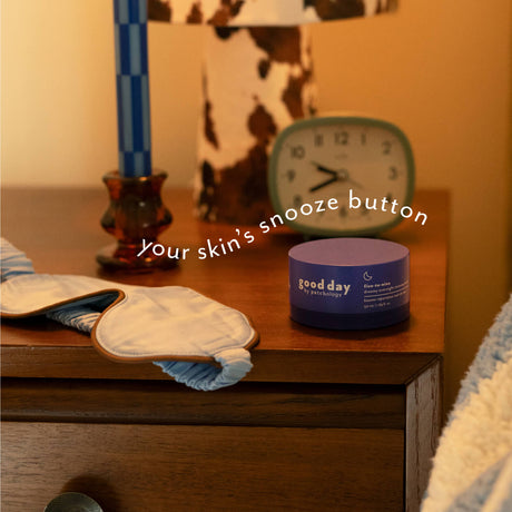 Five-to-Nine Dreamy Overnight Recovery Balm on a bedside table beside a sleep mask and alarm clock.