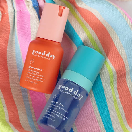Two Good Day skincare bottles with glow potion and Crystal Clear facial mist, resting on a pastel striped fabric background.
