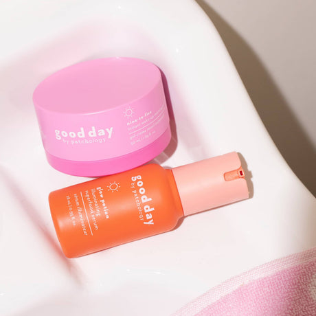 Two skincare duo glow potion and nine-to-five moisturizer, one in a pink jar and one in an orange pump bottle, arranged on a white ceramic surface.