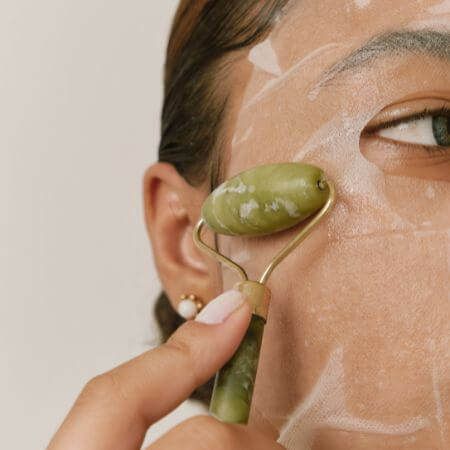 Close-up of a person using a jade roller on their face, with facial mask residue visible.
