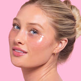 Woman wearing transparent under-eye gel patches with dewy skin against pink background for hydrating skincare use
